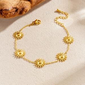 Gold plated stainless steel bracelet with sunflower charms on a textured surface
