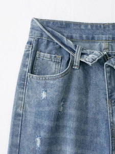 Dettaglio ravvicinato di jeans blu slavato con strappi decorativi e bottoni in metallo