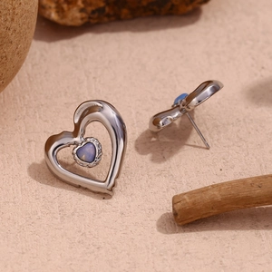 Close-up of silver hollow heart stud earrings with blue gemstone on natural stone