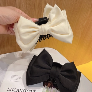 Detail of premium satin bow hair claws in cream and black for elegant hairstyles