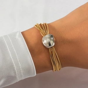 Detail view of multi-layered gold chain bracelet with polished silver sphere on wrist