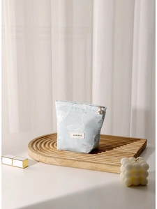 Light blue swan jacquard cosmetic bag with gold zipper on a minimalist wood tray