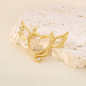 Detailed shot of golden heart pendant with angel wing and devil horn on stone