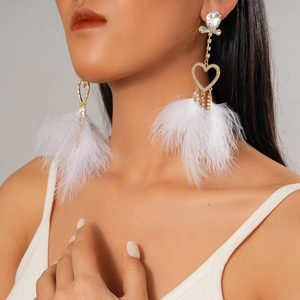 Macro detail of model wearing gold heart earrings with white feathers and rhinestones