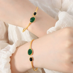 Retro gold cuff bracelet with black and green onyx stones worn by a model on white silk