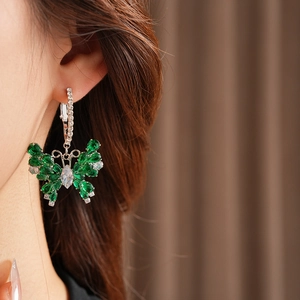 Detail view of a silver butterfly hoop earring with green zircons worn by a model