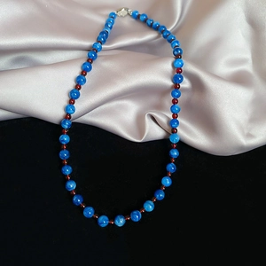 Detail of blue jade beaded necklace with reddish spacers on silver and black fabric