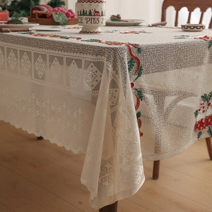 Detail of cream lace tablecloth with festive red ribbon and holly Christmas embroidery