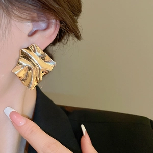 Close-up of a large gold irregular pleated earring on model in a sleek black suit