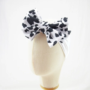 Detailed view of baby headband with a large cow print bow on soft white elastic nylon band