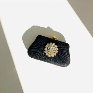 Close-up of elegant black pleated evening clutch with crystal petal ornament and gold clasp