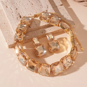 Detail of champagne square crystal necklace and earrings set on beige stone background