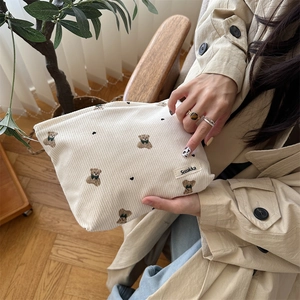 Detail showing the white corduroy texture and cute bear pattern on a handheld cosmetic bag