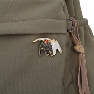 Macro shot of black and white angel wings enamel pin on a green canvas backpack