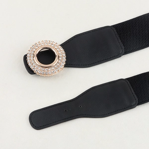 Close-up of black elastic waist belt featuring a gold circular buckle with rhinestone accents