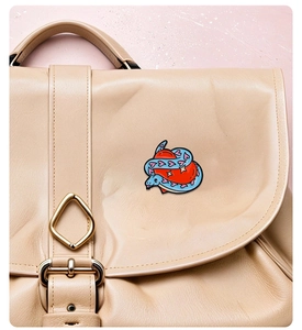 Detail of blue snake enamel pin with pink hearts pinned on a beige leather bag flap