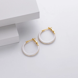 Detail of minimalist 925 sterling silver gold-plated hoop earrings on a white cube