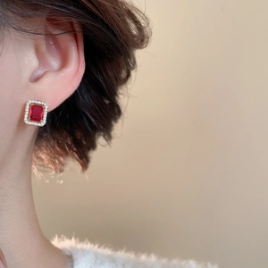 Detail of red emerald cut stone earring with white zircon halo on a gold finish