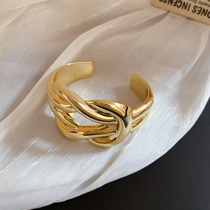Detailed view of wide golden twisted knot open bangle on soft white textured fabric