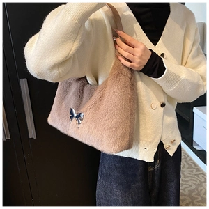 Close-up of light brown plush handbag featuring a silver butterfly buckle and soft fur texture