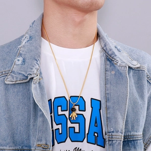 Detail view of golden astronaut pendant on snake chain necklace worn by a male model