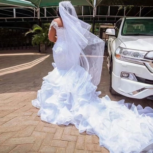 Elegant white mermaid lace wedding dress with voluminous ruffled train and beaded veil