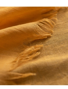 Detail eines warmgelben Schals mit hochwertiger Leinentextur und feinen Fransenkanten
