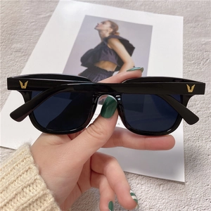 Detail of black square sunglasses with a gold V-shaped logo on the temple over a magazine
