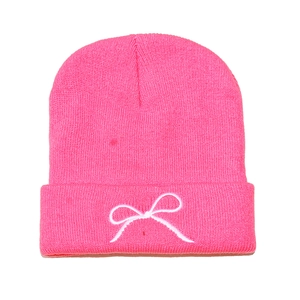 Detailed close-up of bright pink knitted beanie featuring white bow embroidery on cuff