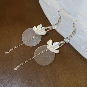 Close-up of silver tassel earrings with white flower and shell-textured round pendant