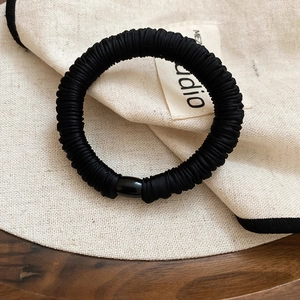 Detail of a thick black ruched hair tie featuring a polished cylindrical buckle accessory