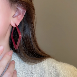 Detail of burgundy geometric rhombus earring worn by a model with glossy finish