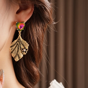 Macro shot of gold leaf earrings featuring a heart gemstone, black beads and pearl detail
