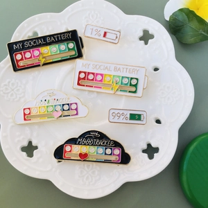 Detailed view of enamel social battery and mood tracker pins on a white ceramic plate
