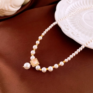 Macro shot of pearl necklace with square zircon pendant on elegant silk fabric