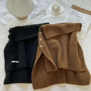 Detail view of knitted wool ponchos in black and brown with decorative side buttons