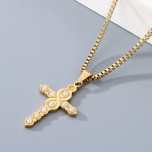 Macro detail of golden cross necklace with inlaid white imitation pearls on box chain