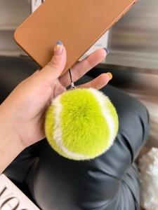 Detailed view of yellow plush tennis ball keychain held against a lifestyle background