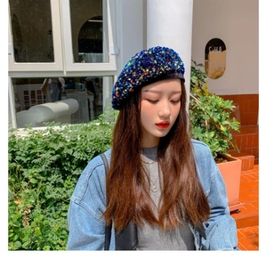 Detail shot of a sparkly blue sequin beret hat worn by a model in outdoor daylight