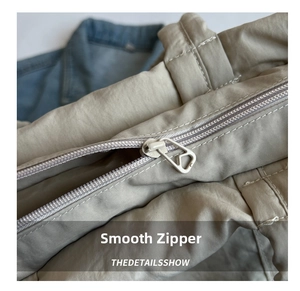 Close-up of a smooth silver metal zipper on a beige nylon tote bag with fine texture