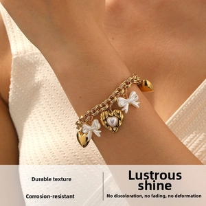 Detail of gold-plated thick chain bracelet with heart charms and white bows on a wrist