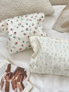 Floral lace makeup bag with fringe detail and vintage aesthetic on a soft white bed