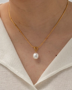 Detail of elegant gold chain necklace with white freshwater pearl pendant on a model