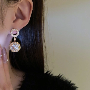 Close-up of gold hollow round earrings with pearl pendant on a model's ear