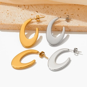 Polished gold and silver C-shaped oval stud earrings on minimalist stone background