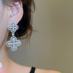 Close-up of elegant silver four-leaf clover drop earrings with pavé zircon crystals on a model