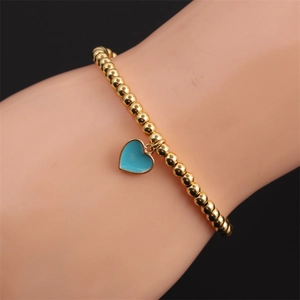 Close-up of a gold-plated beaded bracelet featuring a vibrant blue heart charm on a wrist