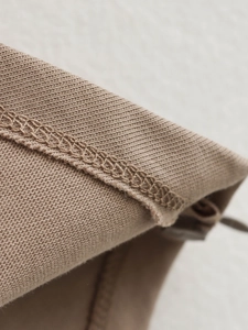 Macro shot showing high-quality overlock stitching on warm beige knit top edges