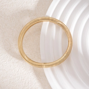 Vue détaillée d'un bracelet doré texturé en spirale sur un plateau en céramique blanc