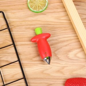 Stainless steel strawberry huller with red handle shown on a rustic wooden tabletop